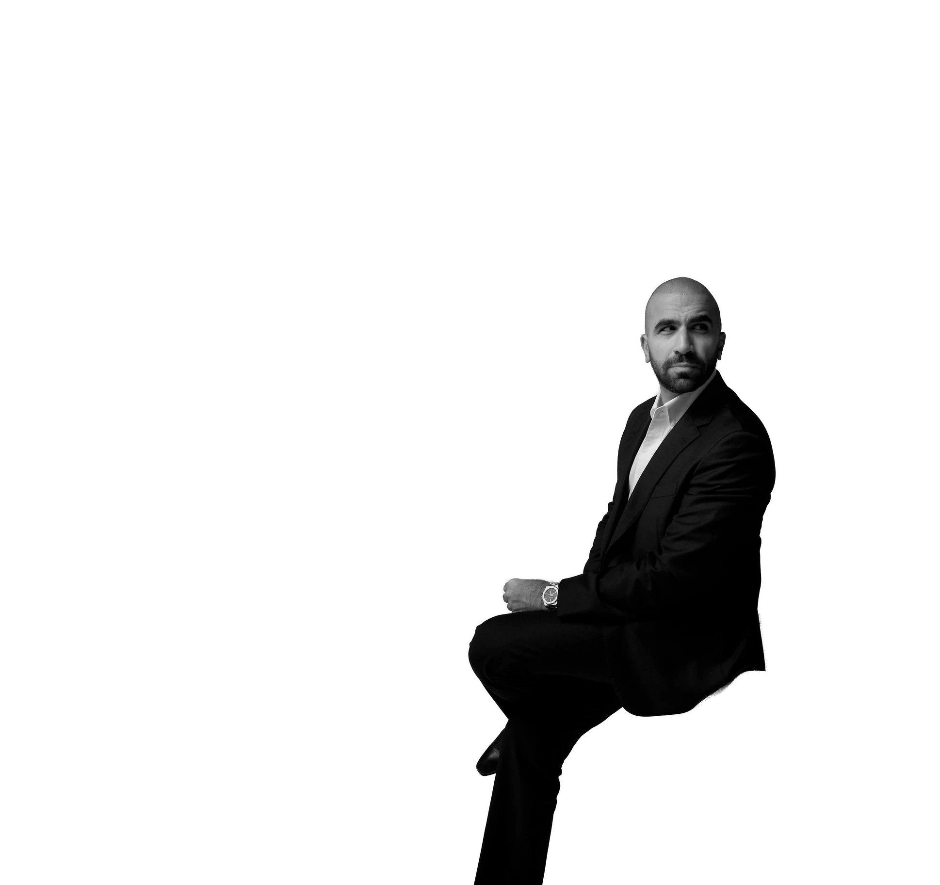 Ahmed El-Gamal seated, looking over his shoulder, in a dark suit and white shirt